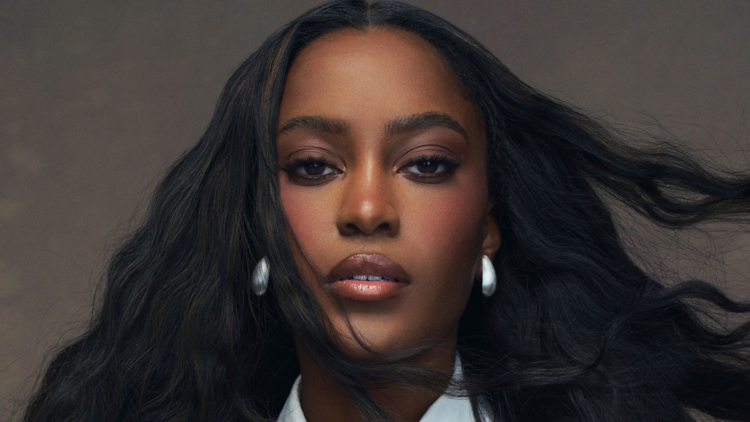 Ciara Miller wears a white shirt and tie. Her hair is styled in waves.