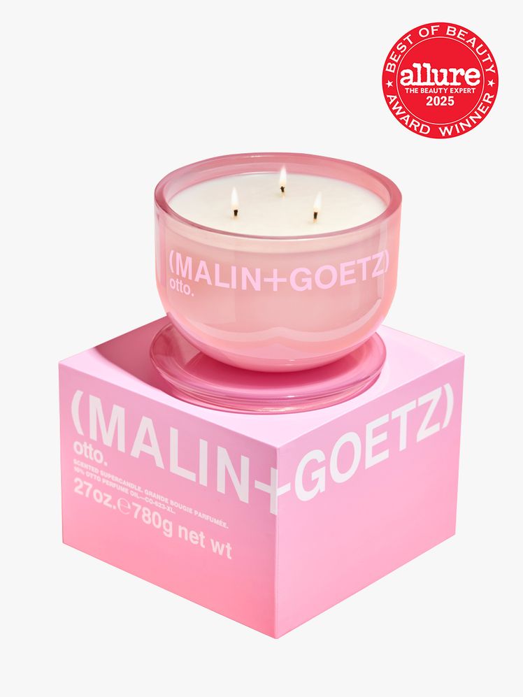 Malin  Goetz otto supercandle in clear pink container atop branded pink box packaging on light gray background with red...