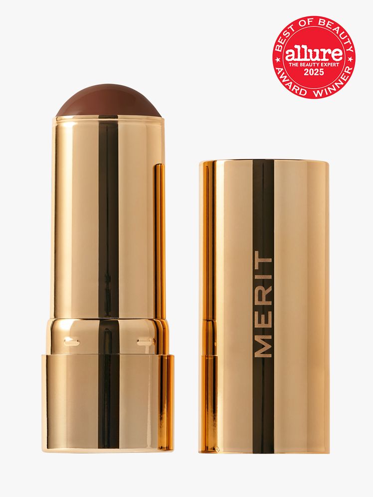 Merit Bronze Balm in branded gold twist up applicator on light gray background with red Allure Best of Beauty seal in...