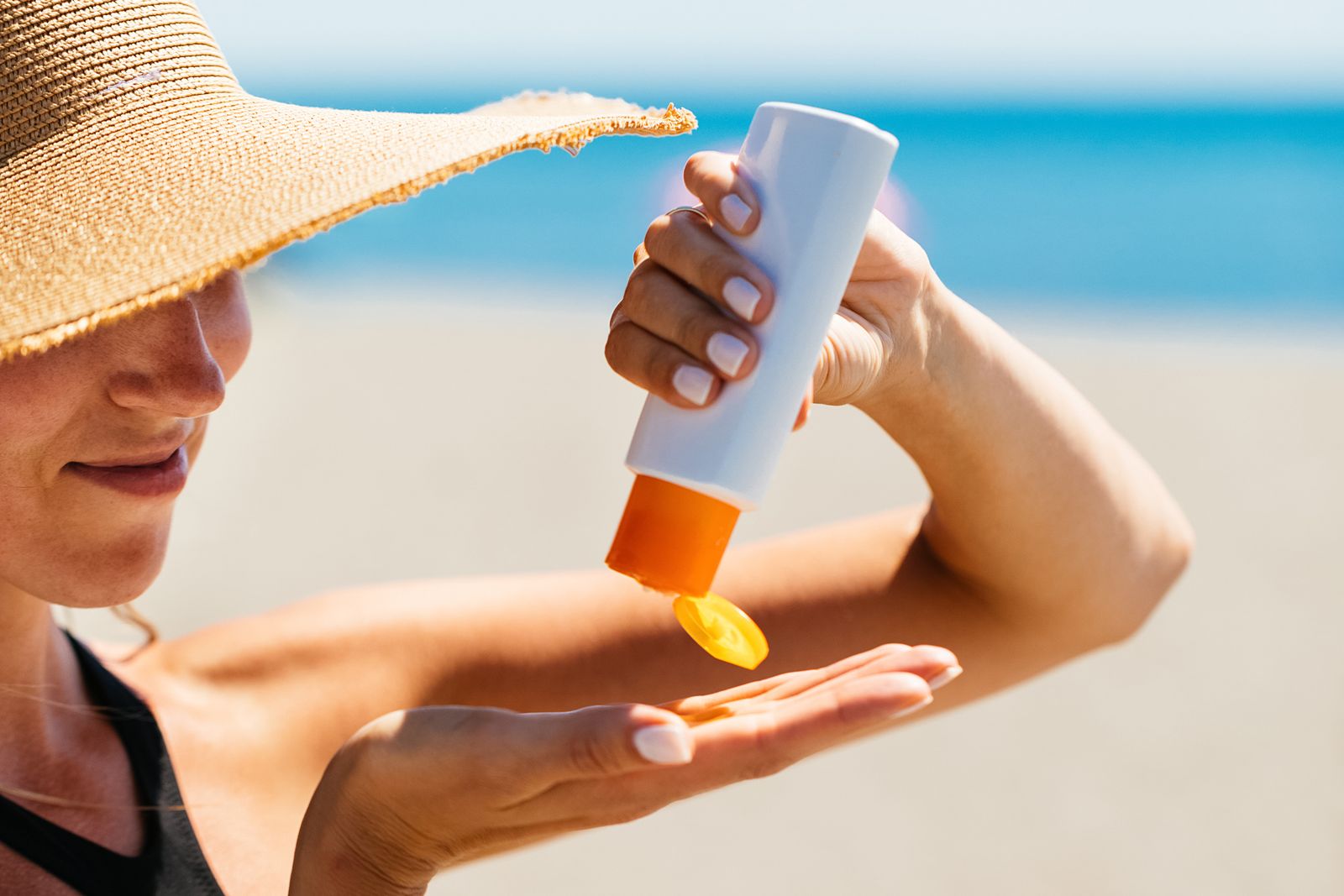 woman on the beach squirting sunscreen from a bottle onto her right hand